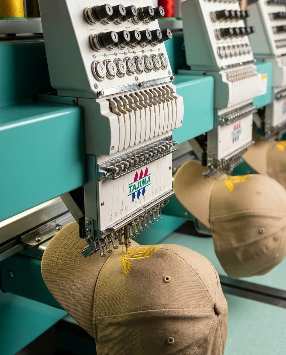 A multi-head Tajima embroidery machine running multiple navy caps